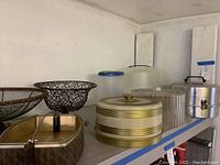 Shelf with metal cake carriers, decorative containers, hard plastic cake carrier.