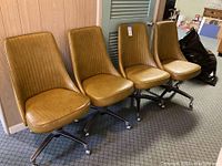 Four matching vintage yellow office chairs with vertical stitched design, metal base with caster wheels, arranged side by side.