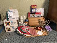 Full lot overview showing bread box, jelly jar boxes, cups, forks, mandolin slicer box, butterfly decor, linens and trivets on woven tray.