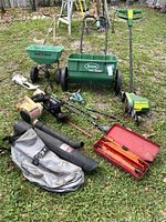 Full lot showing various yard tools including the leaf blower with collection bag, electric edger, fertilizer spreader, hazard lights, and toolbox with hand tools.