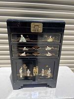 Front view of black lacquer chest with top locking clasp, two drawers and lower doors