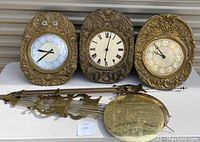 Three brass clock cases side by side with pendulum assembly laid in front