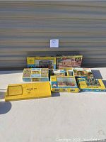 Photo showing eight boxed HO scale building kits arranged on a white table, including Minikits, Atlas, RHM, and an envelope style kit.