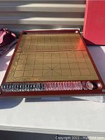 Open folding wooden Chinese chessboard with gold-colored play surface and black grid lines, showing two rows of crystal glass chess pieces arranged in front - transparent on one side and black on the other.