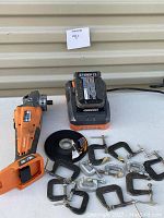 Photo showing Ridgid cordless grinder, battery charger with battery, grinding wheel, and multiple vintage metal C-clamps on a white surface.
