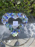 Top-down view of heart-shaped piece made from multi-colored sea glass pieces arranged on a glass table outdoors, showing full shape and distribution of sea glass colors.
