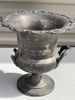 Front view of silver plated trophy vase with engraved inscription and ornate rim details.