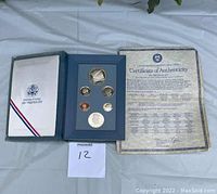 Photo of the open blue presentation folder with six proof coins and the Certificate of Authenticity beside it