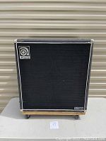 Front view of cabinet showing black grille cloth, Ampeg badge, silver piping and corner protectors.