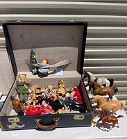 Wide view of open vintage suitcase filled with assorted vintage dolls, including fabric and composition dolls in various costumes and poses, plus multiple Breyer model horses positioned outside the suitcase, varying in color and size, one noted as missing a leg.