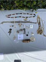 The photo shows a variety of vintage costume jewelry laid out on a table, including several necklaces, multiple bracelets, pairs of clip-on earrings, brooches, and pendants of different styles and materials.