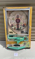 Full front view of wooden-framed pachinko machine with clear playfield, green lever assembly and metal ball tray