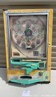 Front view of vintage Nishijin pachinko machine with wooden frame and circular playfield showing metal pins and bumpers. Shows entire device from top to bottom including play control area.