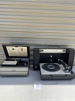 Wide view of two vintage electronic items: on right, black Wildcat record player with tonearm and turntable; on left, Argus slide projector with open lid showing instructions.