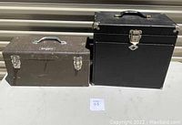 Closed view of brown Union metal toolbox on left and black H. Gerstner machinist chest on right