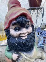 Close-up of heavy, concrete garden gnome with red hat and black beard, showing wear and paint scuffs.