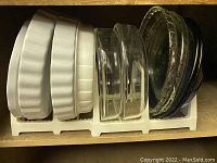Glass and ceramic pie and casserole dishes on rack inside a cabinet.
