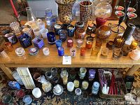 Overview of a table full of assorted candles in glass holders, and a lower shelf containing more candles and candle accessories.