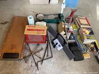 Overview of lot showing mechanic creeper, utility seat, hydraulic floor jack, jack stand, tire irons, crow bars, vintage manuals, cleaning cloth, and other car accessories
