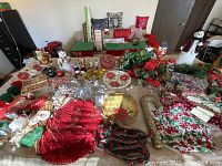 Wide view of table covered with assorted Christmas decorations including figurines, plates, pillows, wreaths, garlands, candles, and wrapping supplies