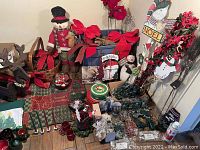 Photo showing assorted Christmas decorations including snowman, bows, greenery, red ornament, wooden cat sign labeled 'Noel', and other holiday decor on table.