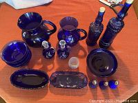 Photo showing entire set of cobalt blue glassware arranged on table, including pitchers, bottles, bowls, decanters, relish dishes, small glass and shakers.
