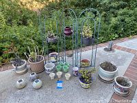 Overview of folding wrought iron plant stand with multiple pots and succulents surrounding it outdoors on tiled surface.