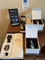 Photo shows four new smart watches in boxes positioned around a working desktop clock showing date, time, weather, temperature, and humidity.