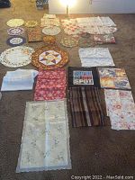 Full view of assorted holiday tablecloths, overlays, and pillow covers spread on carpet showing varied festive patterns and color schemes.