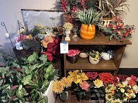 Wide shot of multiple artificial flower arrangements in ceramic pots and wicker baskets on and around a wooden shelf