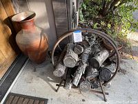 Wide shot showing the large terracotta-style pot next to the curved metal firewood holder filled with firewood.