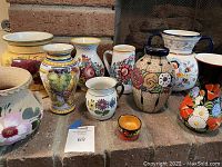 Assorted collection of eight pots and vases with various colorful floral and grapevine patterns displayed on the floor.