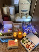 Wide shot of various flameless candles including cream, red, glitter pillars, glass bottles with blue string lights, and boxed tea lights