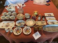 Full overview of the lot on wooden table including tea pot, cups, sugar bowl, creamer, trays, salt and pepper shakers, decorative items.