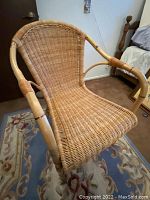 Rattan chair with curved arms and woven seat and back, cushion included, minor rattan damage visible