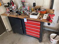 Full front view of the metal tool cabinet with multiple red drawers and various tools and containers on the wooden top surface.