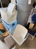 Photo showing a group of storage bins and garbage cans in various sizes and colors including white, blue, green, and brown plastic containers and grey trash cans.