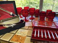 Full lot on tiled surface including ruby red glass goblets and glasses, steak knives, fondue forks with box, and Hamilton Beach electric knife with box and manual.