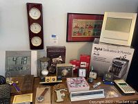 Photo of vintage and new desktop items including weather station instruments, digital clock, coin sorter box, Peanuts framed comic, wristwatch, multiple clocks and decorative items on desk