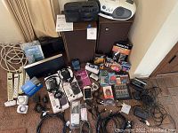 Full lot of vintage electronics and accessories laid out on carpet with visible cords, batteries, radios, recorders, speakers, and clock radio.