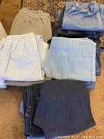 Piles of light blue, white, beige, gray and dark denim pull-on pants including elastic waistbands arrayed on carpet