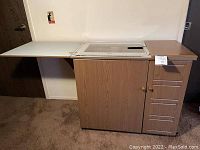 Crafting cart with left side panel extended, showing white expandable side surface, central cabinet with double doors, and five right vertical storage drawers.