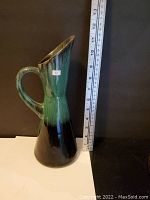 Full view of ceramic pitcher showing its shape and glaze colors with measuring tape indicating height close to 11 inches.