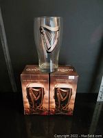 Two clear Guinness pint glasses with harp logo, each in original branded boxes with Halloween themed packaging.