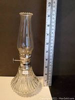 Oil lamp with clear glass chimney and ribbed glass base beside ruler showing height approximately 9 inches.