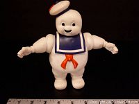 Front view of the Stay Puft Marshmallow Man action figure, showing details of face, sailor outfit, and arms extended, with a measuring ruler in the background for scale showing approximately 7 inches tall.