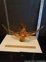 Front angle view of large amber vintage glass dish with chalet style extensions with ruler for scale, approximately 24 inches wide.