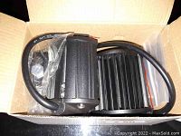 Two black LED light bars inside a cardboard box, showing the finned back and attached wiring cable.