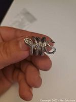 Silver-tone snake ring held between thumb and fingers showing snake head, body and coiled design details.