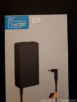 Front of the white box showing a photo of the black power adapter and connector, along with the "AC Charger" label and lot sticker.